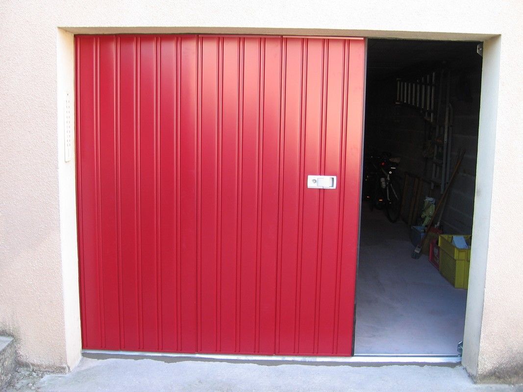 Une porte de garage en métal rouge vif, ondulée verticalement, est partiellement ouverte, révélant un espace de stockage sombre à l'intérieur.