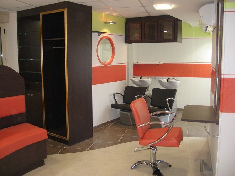 L'intérieur d'un salon de coiffure avec des murs orange et blancs, un meuble de rangement, un fauteuil de coiffure rouge et deux bacs à shampoing.