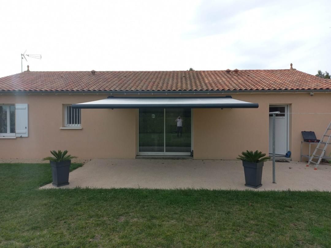 Une maison de plain-pied avec une façade beige, un toit de tuiles et un store banne rétractable récemment installé au-dessus d'une porte.