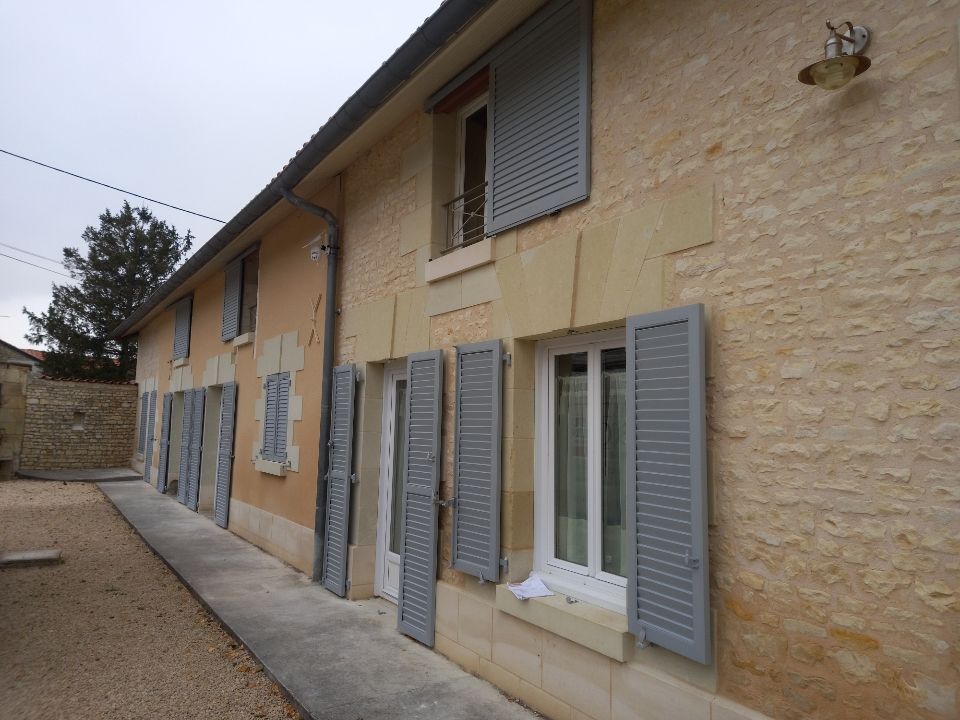 Des volets battants en aluminium gris sur une façade en pierre