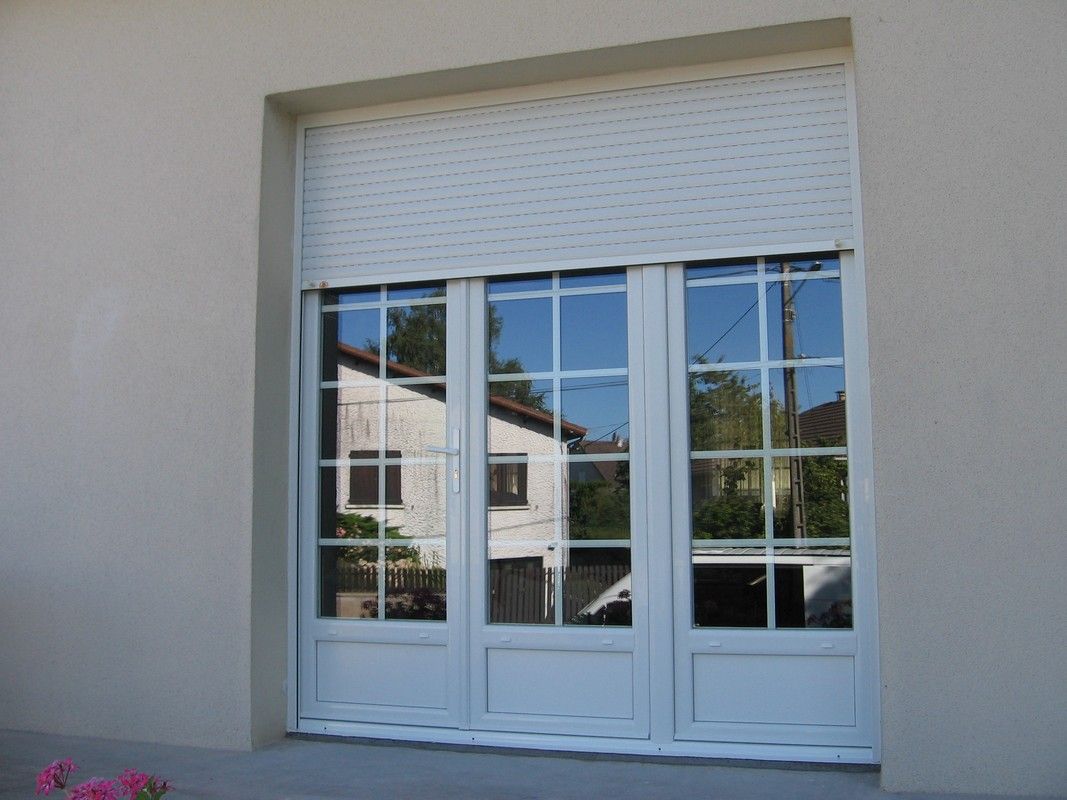 Porte-fenêtre blanche à triple vitrage et à motif quadrillé, encastrée dans un mur beige avec un volet roulant supérieur fermé.