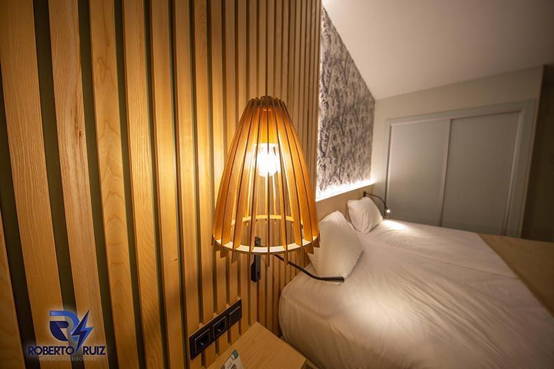 Un dormitorio con cama, mesita de noche, lámpara y pared de madera.