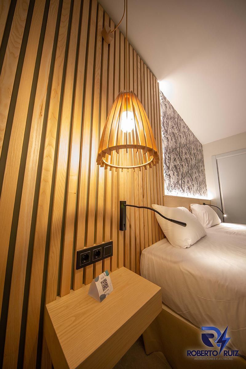 Un dormitorio con cama, mesita de noche, lámpara y pared de madera.