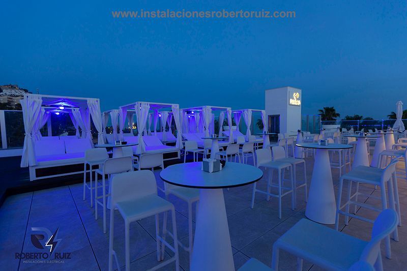 Una fila de mesas y sillas en una azotea con luces azules.