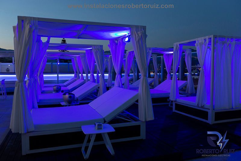 Una fila de sillones bajo toldos con luces violetas.