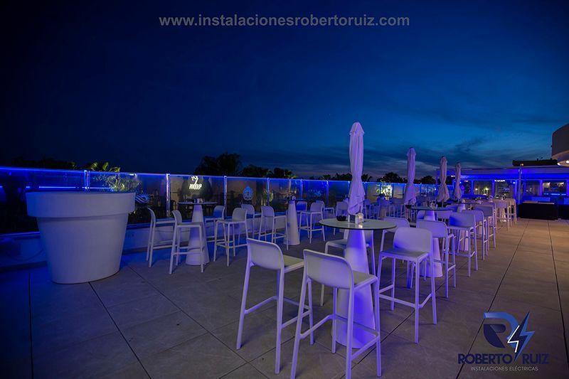 Una fila de mesas y sillas en una azotea por la noche.