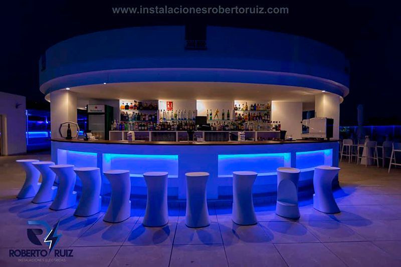 Un bar con luces azules y taburetes delante.