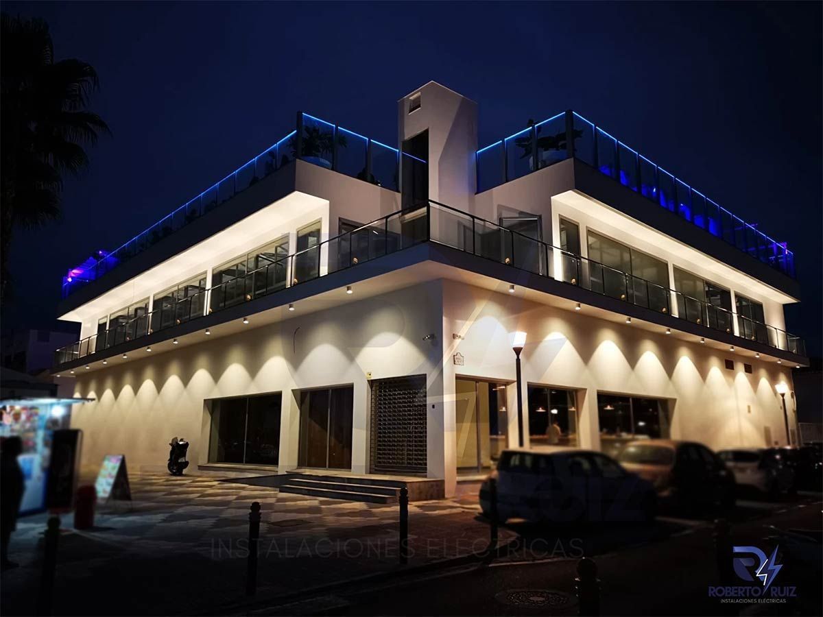 Un gran edificio blanco está iluminado por la noche con coches aparcados delante de él.