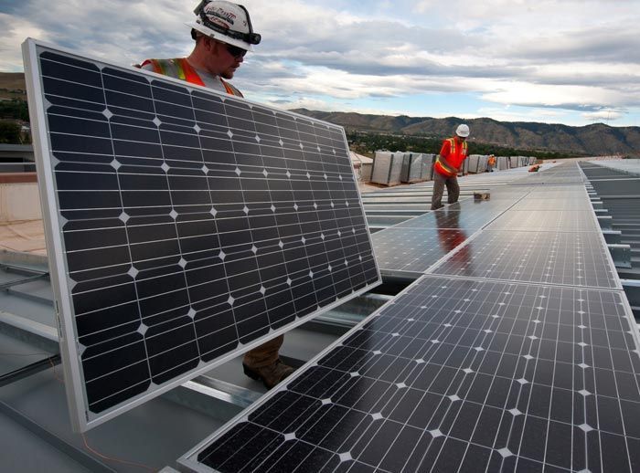 Dos hombres están instalando paneles solares en el tejado de un edificio.
