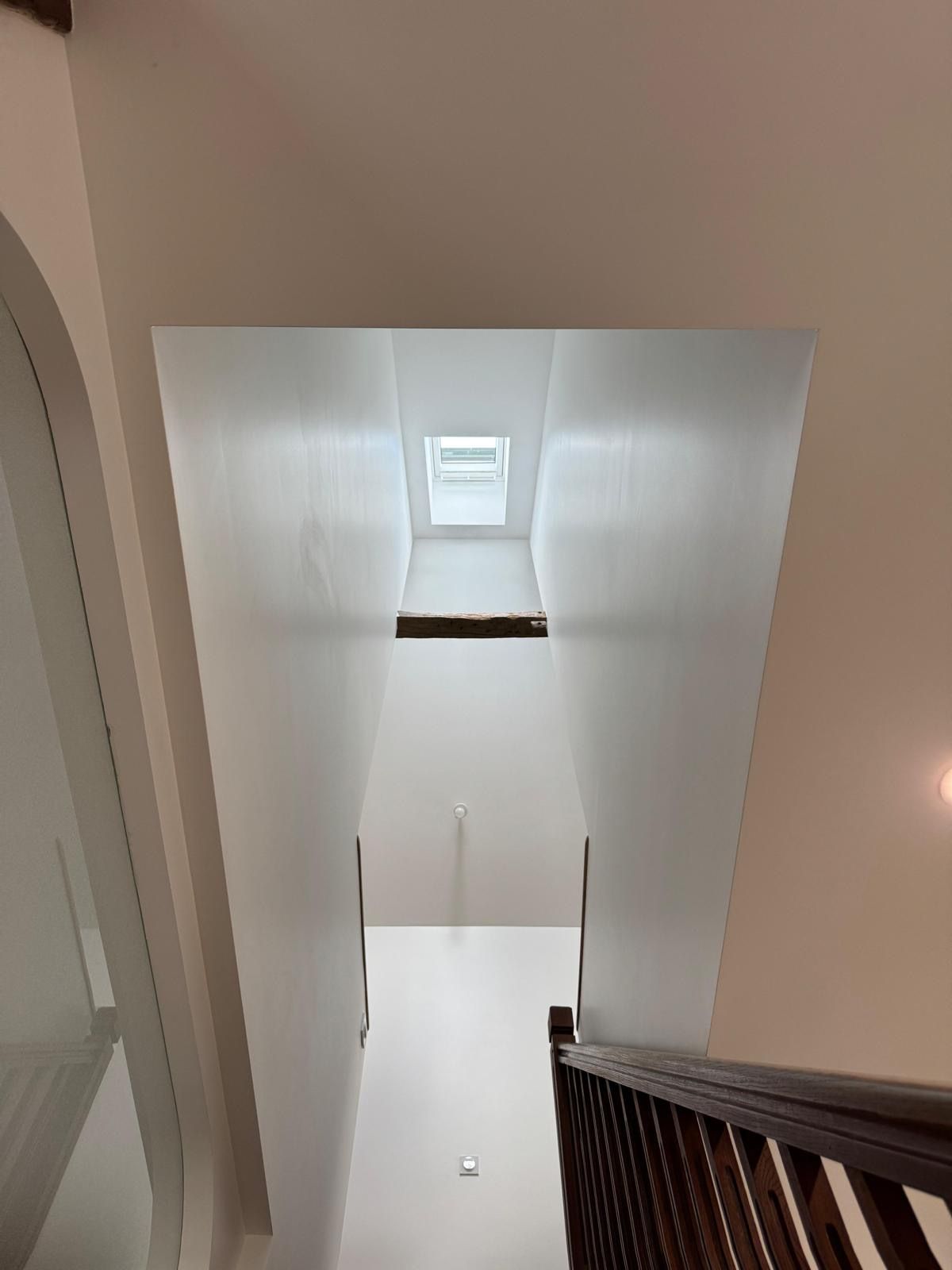 Cage d’escalier minimaliste avec parquet bois, verrière et fenêtre de toit.