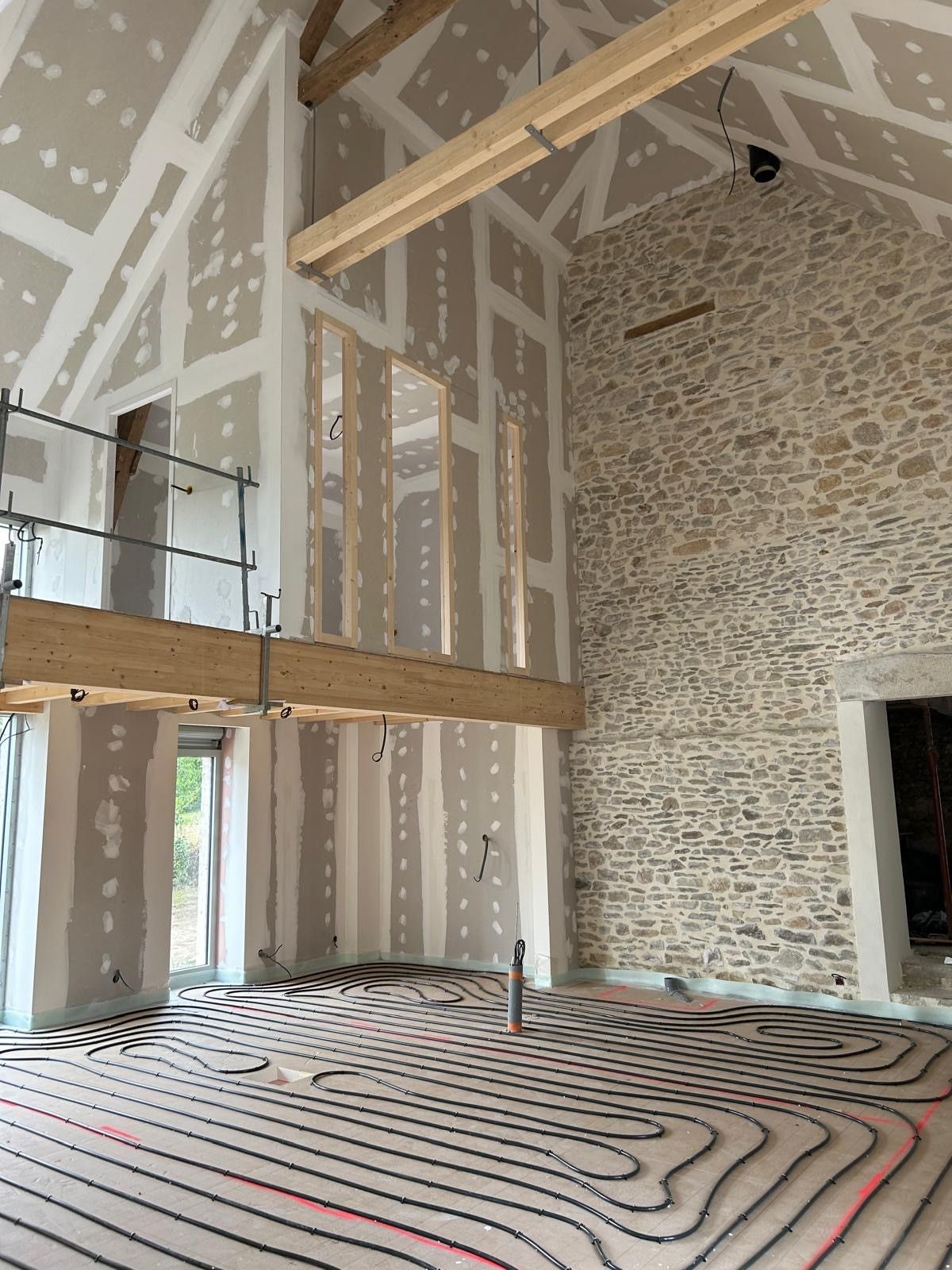 Intérieur d'une pièce rénovée avec mur en pierre apparente, cloisons sèches, poutre de mezzanine et chauffage au sol.