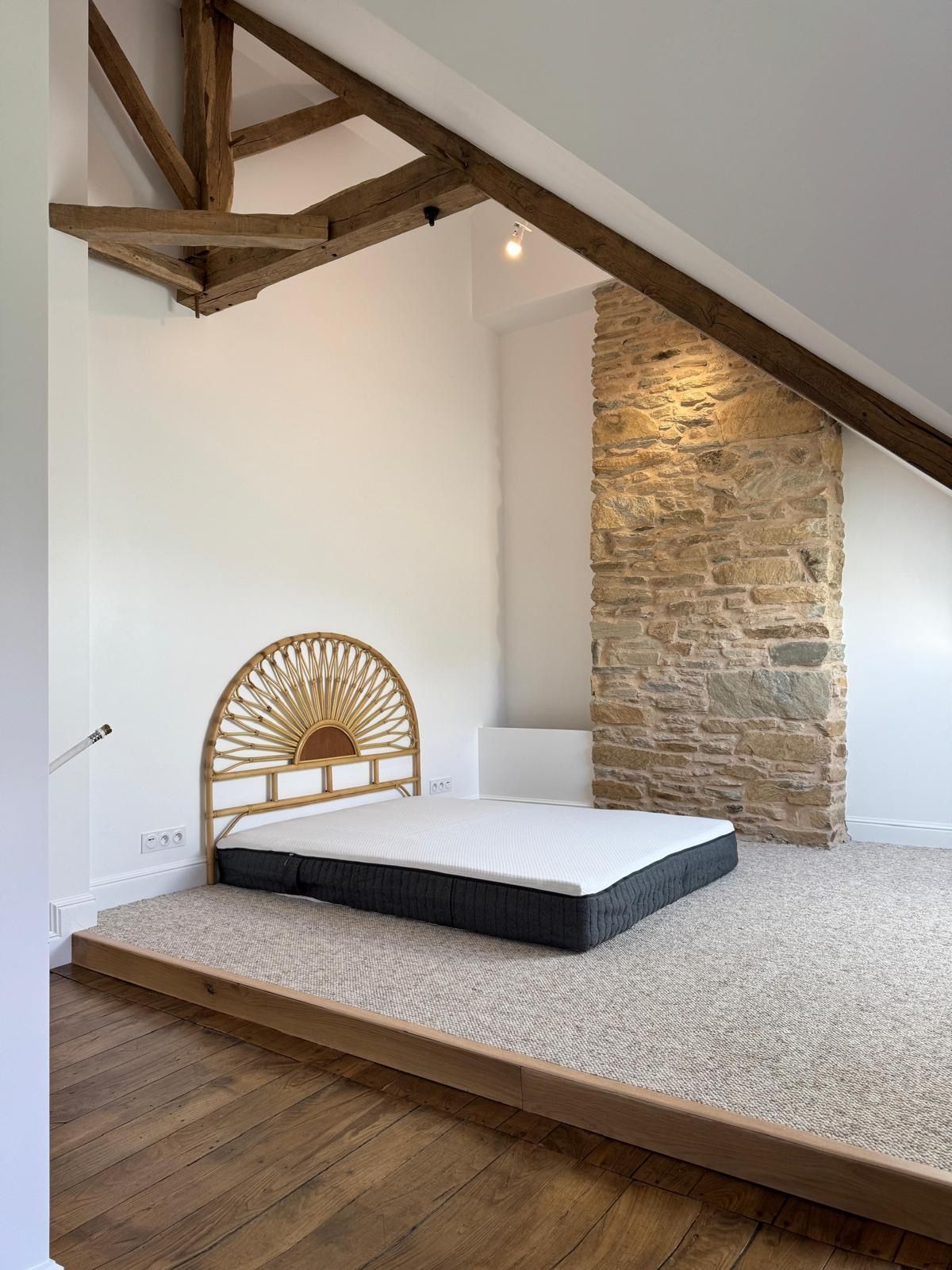 Intérieur d'une maison en construction avec poutres de toit apparentes, cloisons sèches et murs non finis.