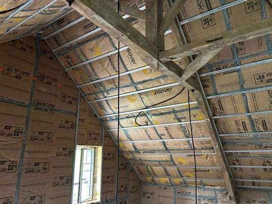 Plafond du couloir partiellement fini avec isolation apparente, poutres en bois et une fenêtre au fond.