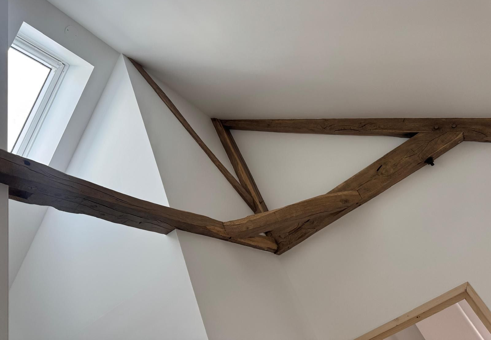 Poutres apparentes au plafond d'une pièce blanche avec un puits de lumière.
