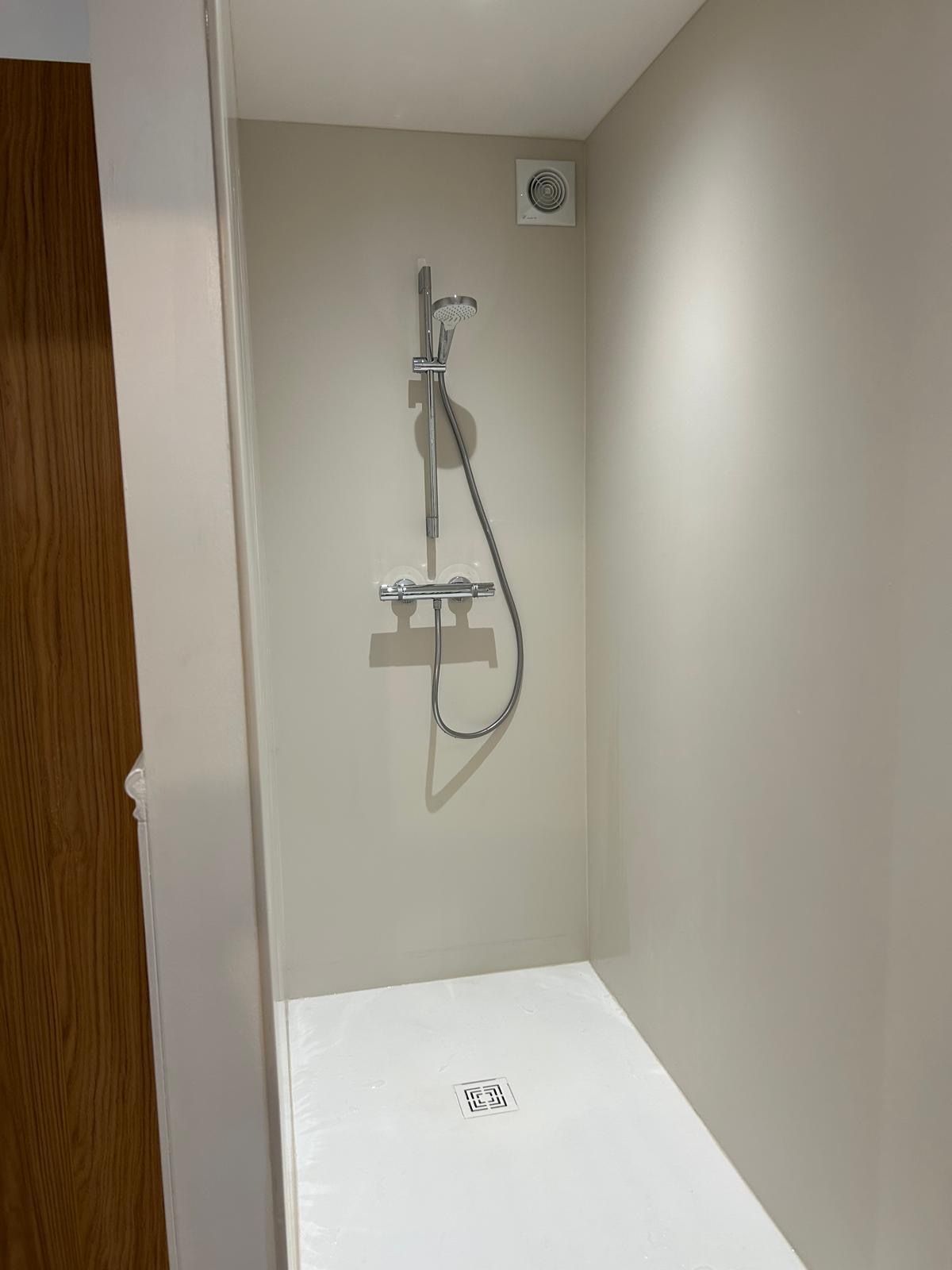 Détail d’une chambre chaleureuse avec lampe murale, tapisserie motif feuillage et mobilier en bois.