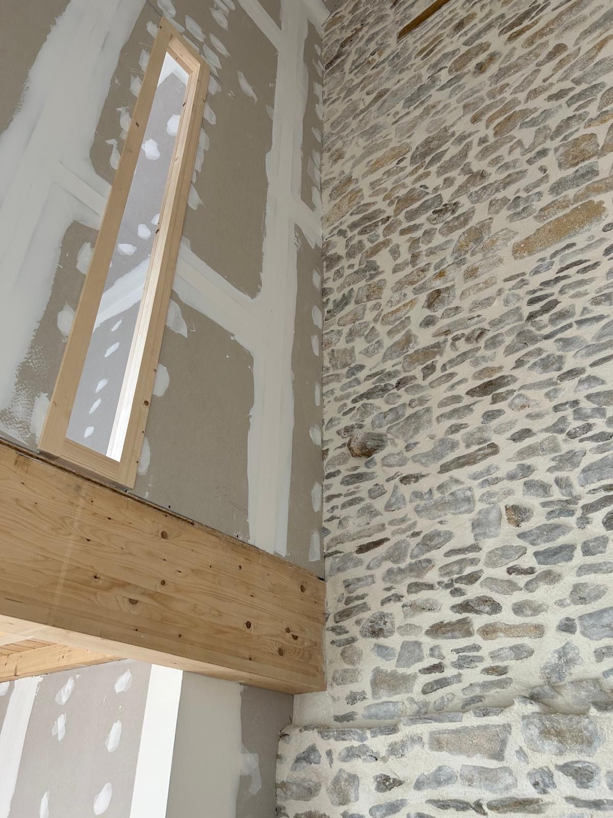 Mur en pierre et cloisons sèches non finies avec joints collés.