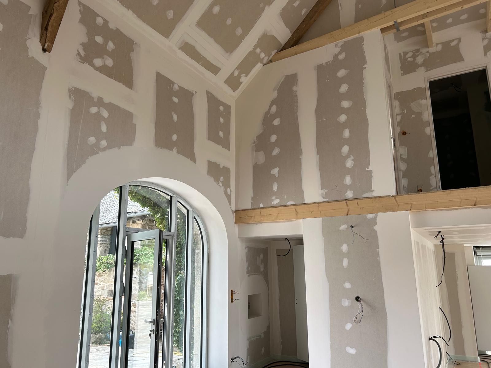 Intérieur en cours de rénovation avec cloisons sèches, porte cintrée et charpente apparente.
