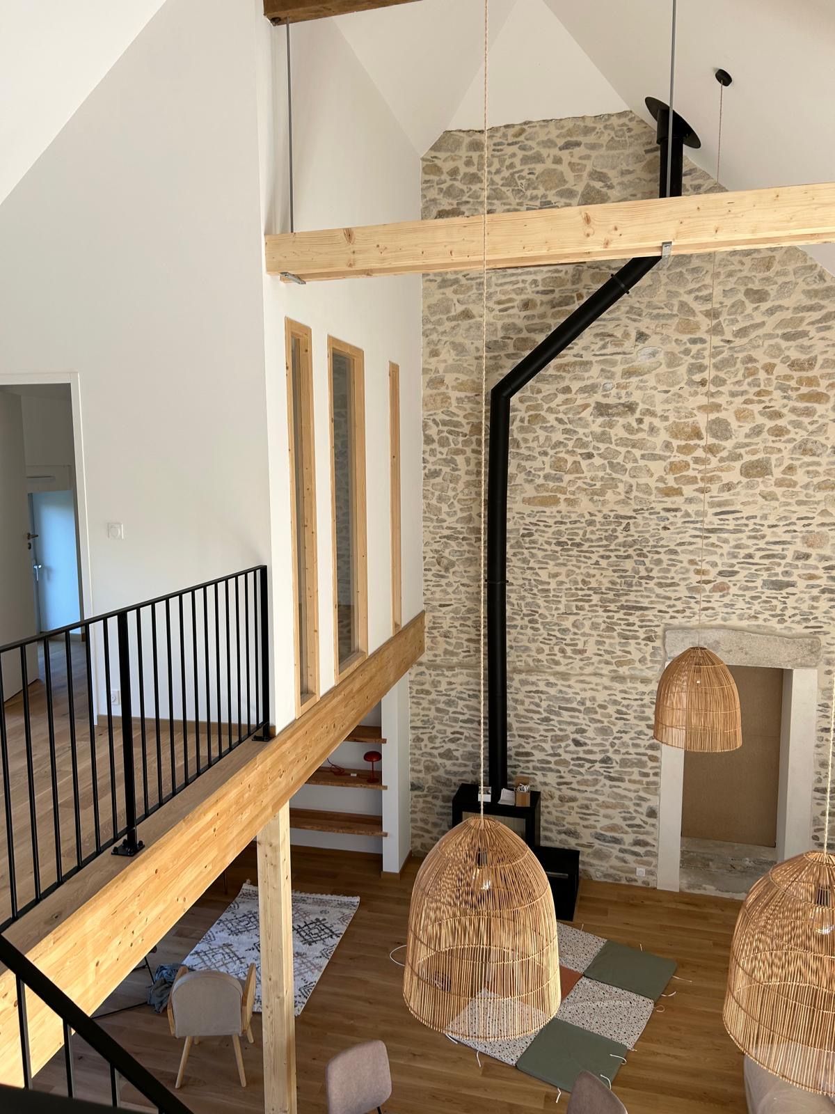 Salon de style loft avec mur en pierre, poêle à bois noir et suspensions lumineuses tressées.