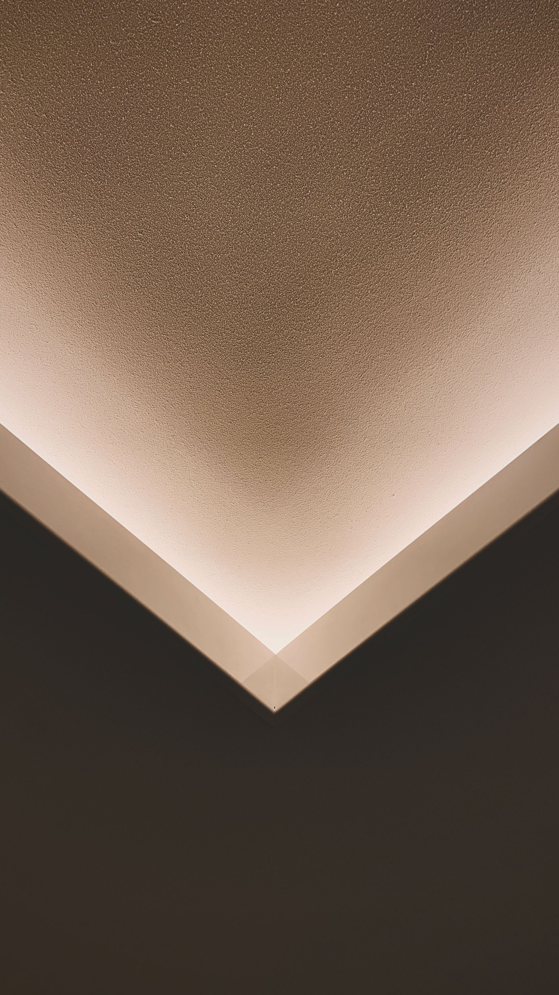 Vue en contre-plongée d'un coin de plafond beige texturé avec éclairage indirect chaleureux.