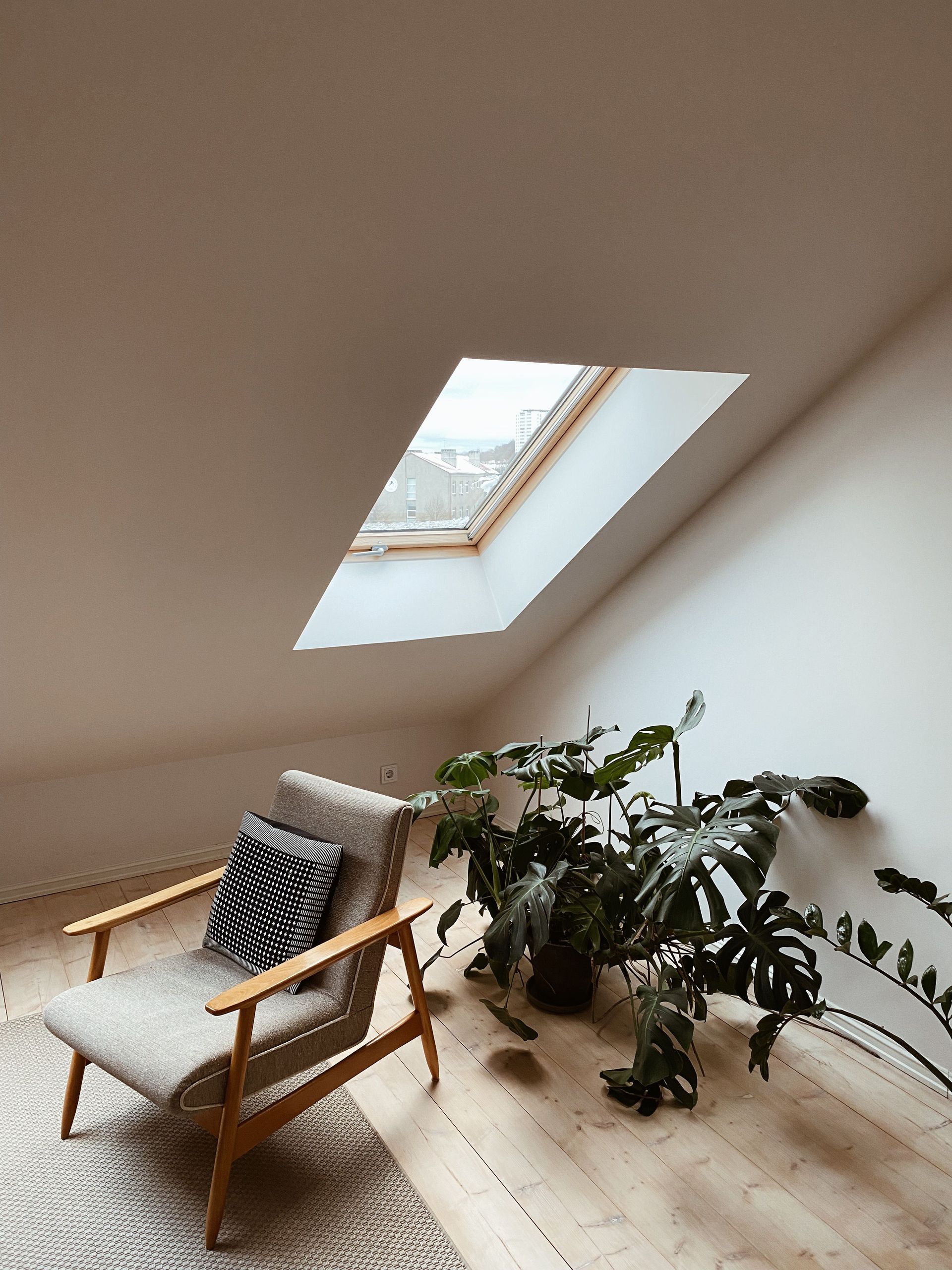 Coin salon minimaliste sous les combles avec une chaise en bois, un coussin rayé, une plante en pot et un puits de lumière.