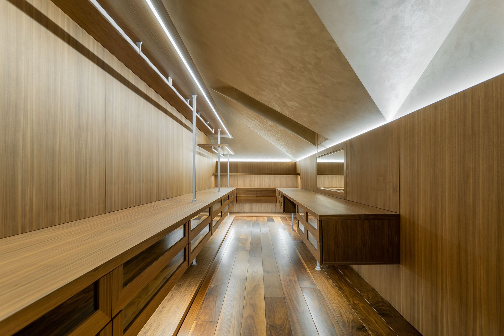 Dressing en bois sur mesure avec parquet et rangements dans une pièce sous pente, avec éclairage LED.