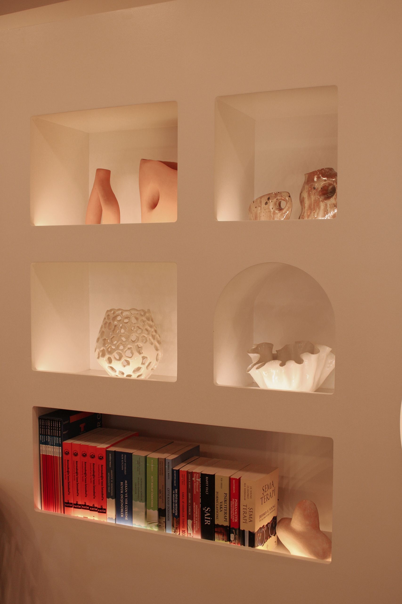Niche murale avec étagères à éclairage tamisé contenant des objets de décoration et des livres.