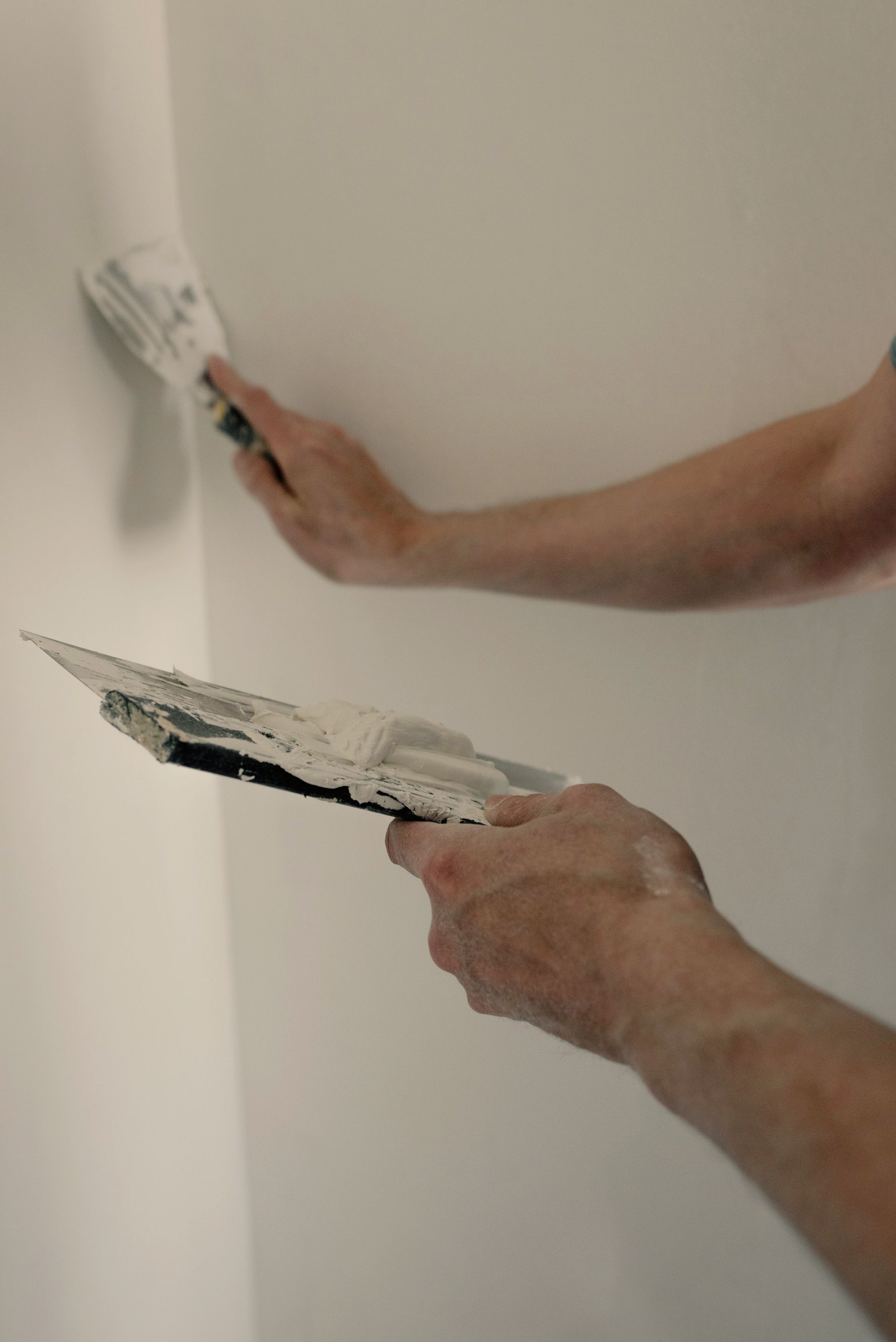 Un ouvrier lisse de l'enduit sur un mur à l'aide d'un couteau à mastic et d'une truelle.