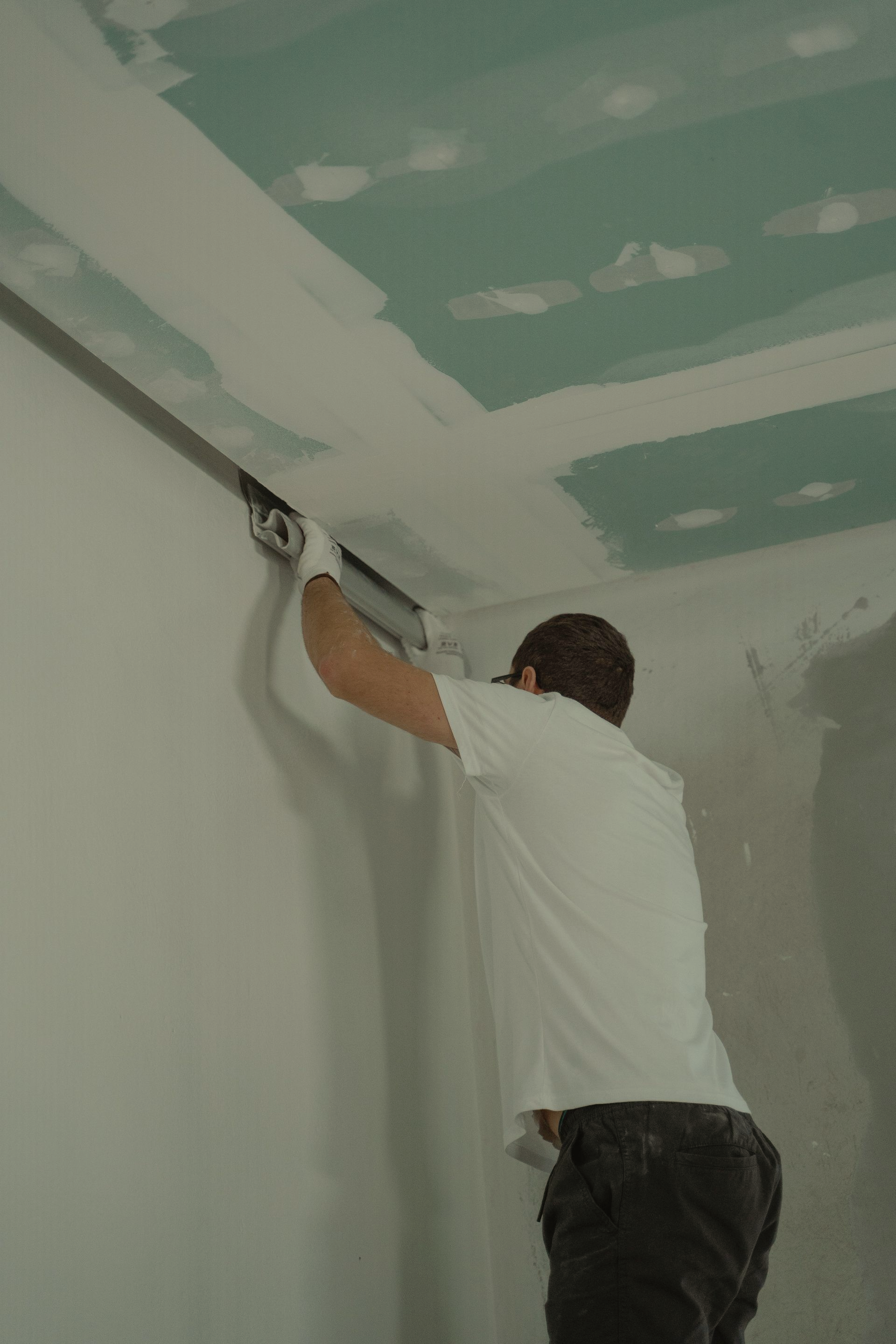 Un plaquiste ponce un mur dans une pièce en rénovation, avec des plaques de placo.