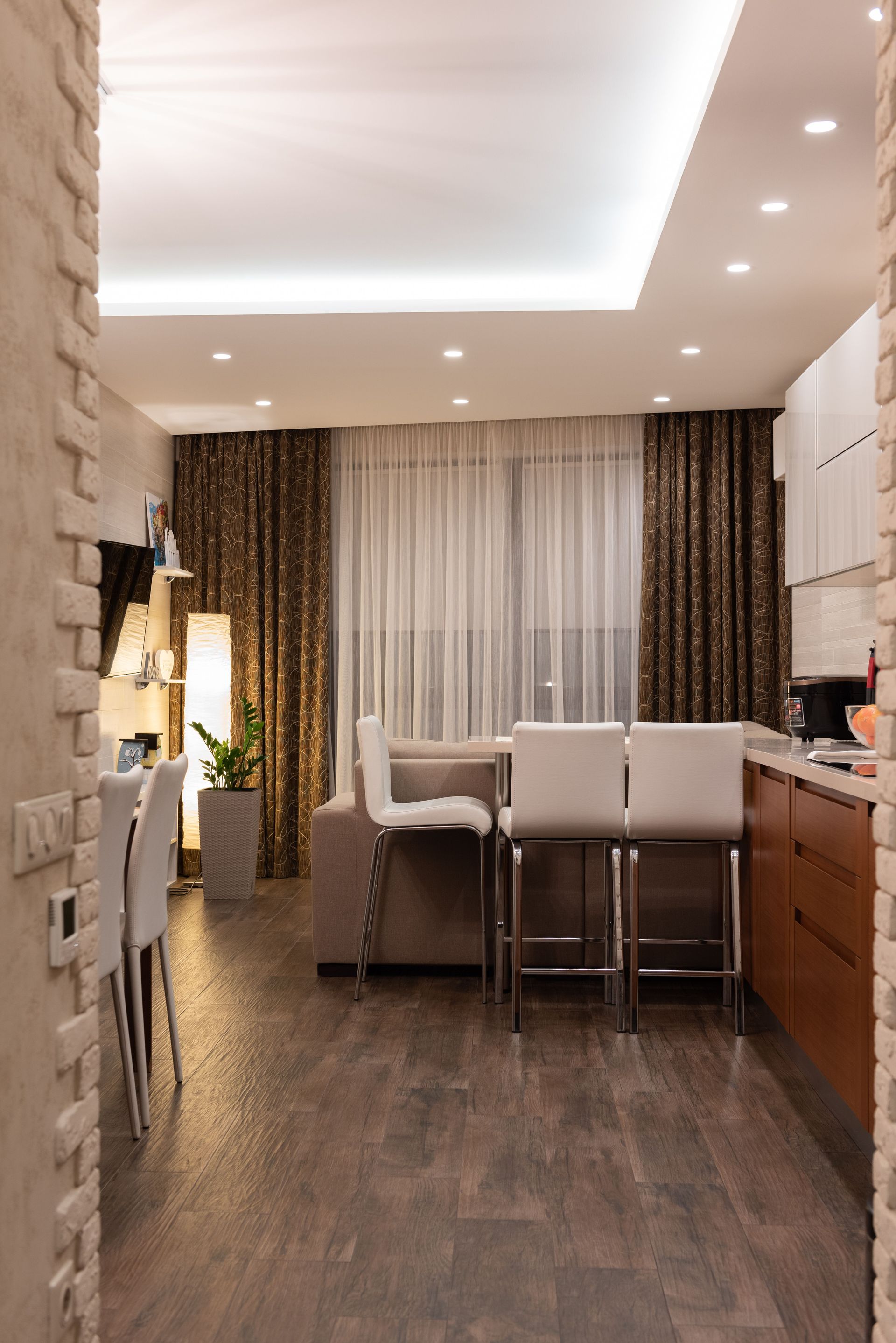 Pièce de vie moderne avec cuisine ouverte, tabourets de bar, parquet et luminaire intégrés dans un faux-plafond.