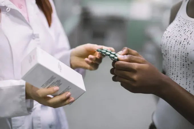 Farmacéutico entrega un blíster de medicamentos a un cliente en el mostrador de una farmacia.