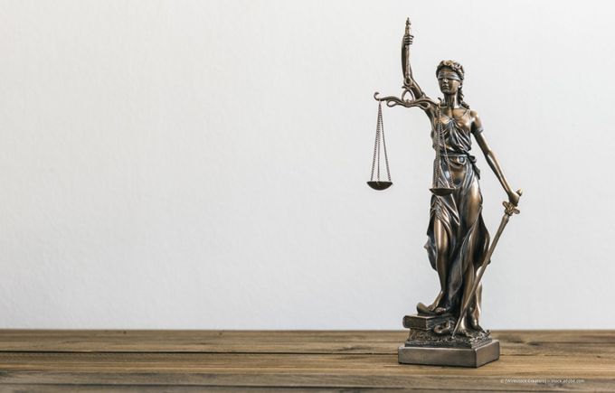 Zwei Personen diskutieren in einem Anwaltsbüro über eine Waage.
