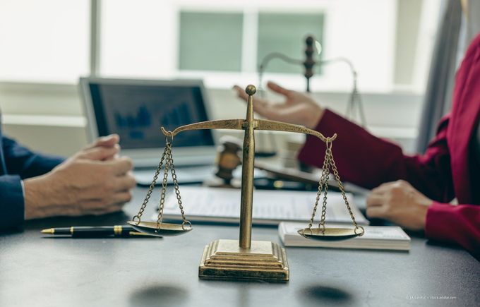 Zwei Personen diskutieren in einem Anwaltsbüro über eine Waage.