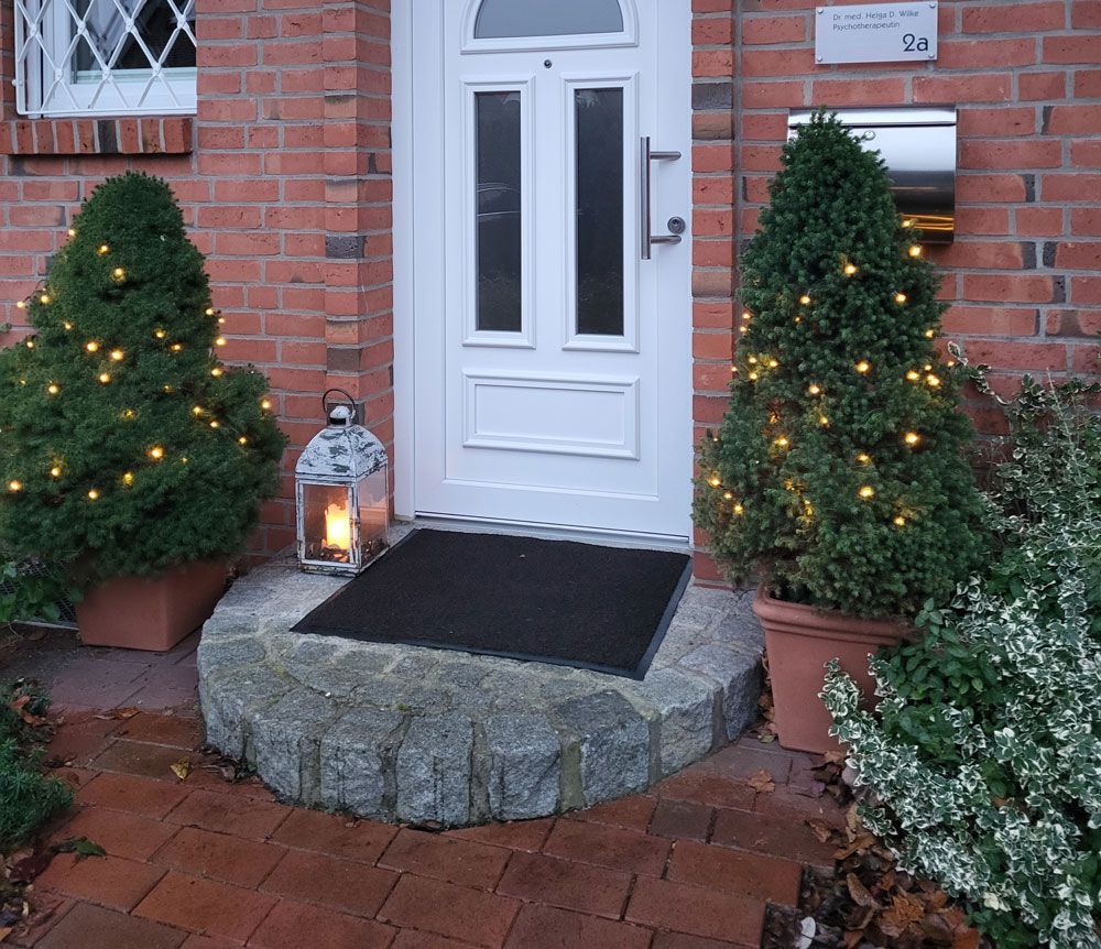 Ein Backsteinhaus mit einer weißen Tür und rosa Blumen davor.