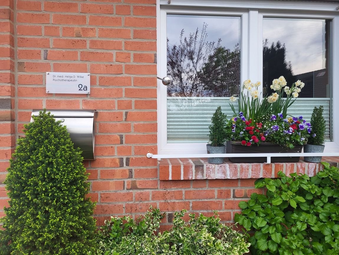 Ein Backsteinhaus mit einer weißen Tür und rosa Blumen davor.