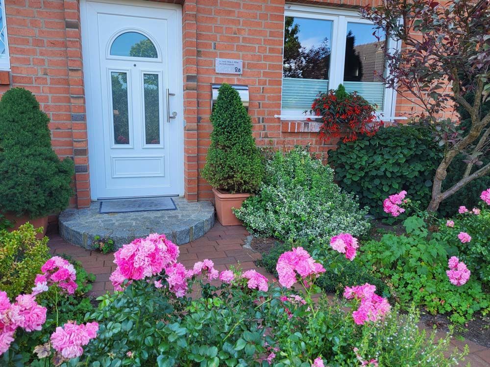 Ein Backsteinhaus mit einer weißen Tür und rosa Blumen davor.