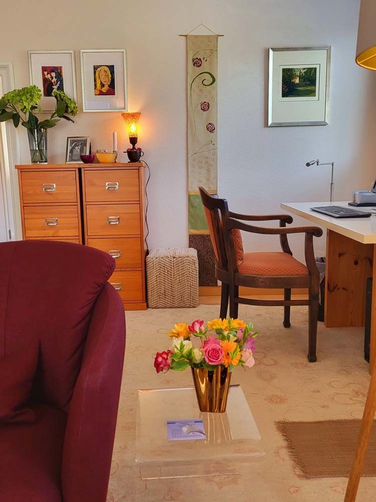 Ein Wohnzimmer mit einem Stuhl, einem Schreibtisch und einer Vase mit Blumen