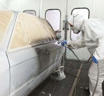 Un hombre está pintando con aerosol un automóvil en una cabina de pintura.