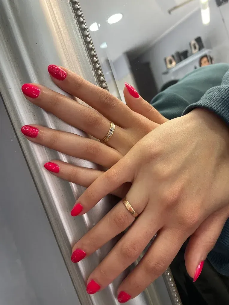 Manos con uñas de color rosa brillante y anillos de oro descansando sobre un espejo junto a una manga verde.