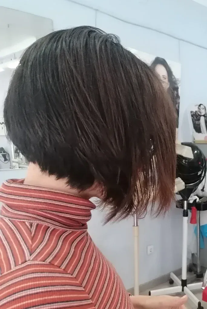 Vista lateral de una persona con un corte de pelo bob corto y oscuro y una camisa de rayas rojas en un salón de belleza.