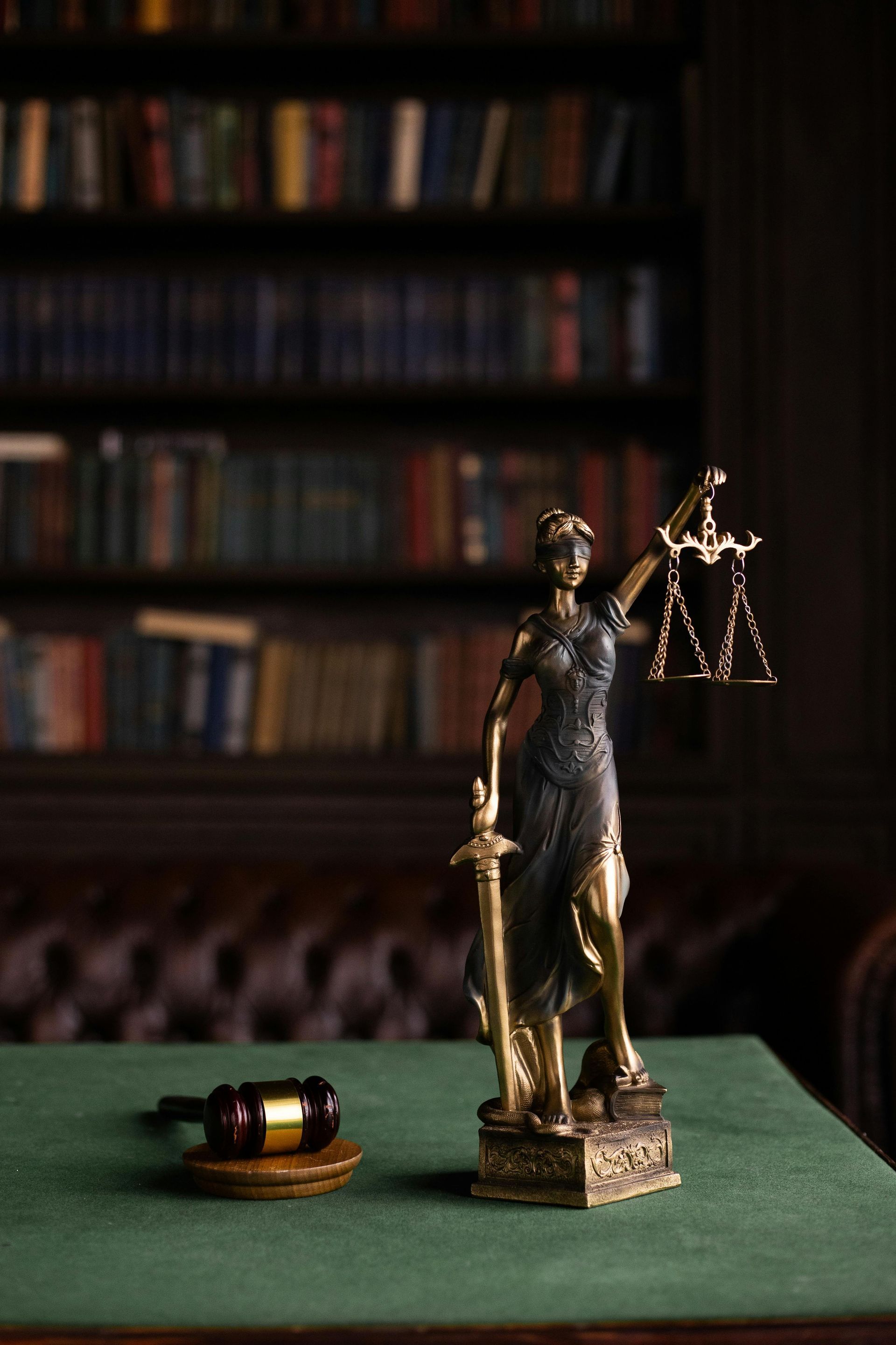 Statue de la Justice avec balance et maillet sur un bureau vert dans une bibliothèque de droit
