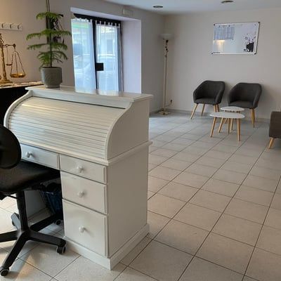 Espace d'accueil minimaliste avec bureau blanc, chaises noires, sol carrelé et porte coulissante en verre.