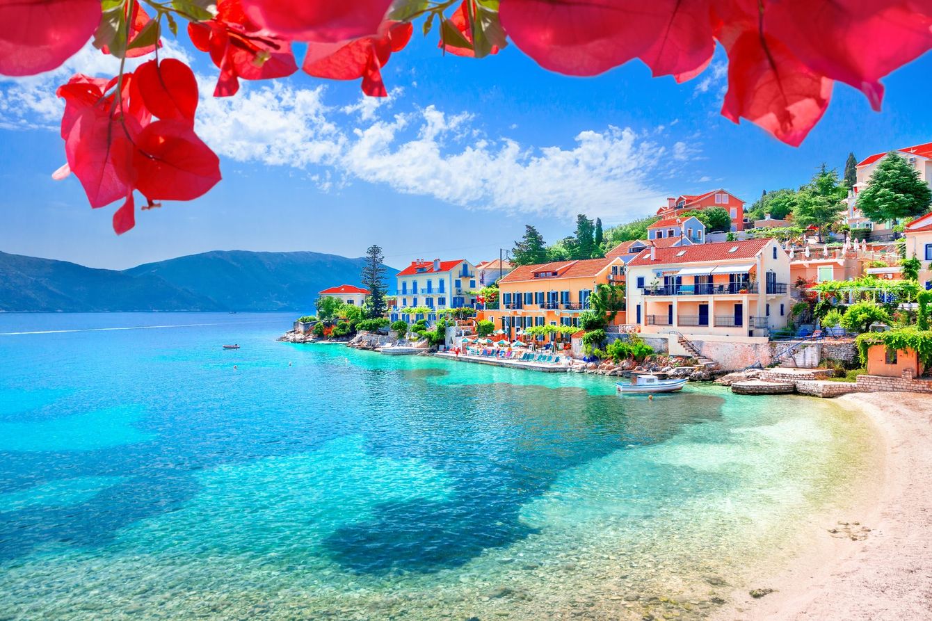 A beach with houses and flowers in the foreground and a body of water in the background.
