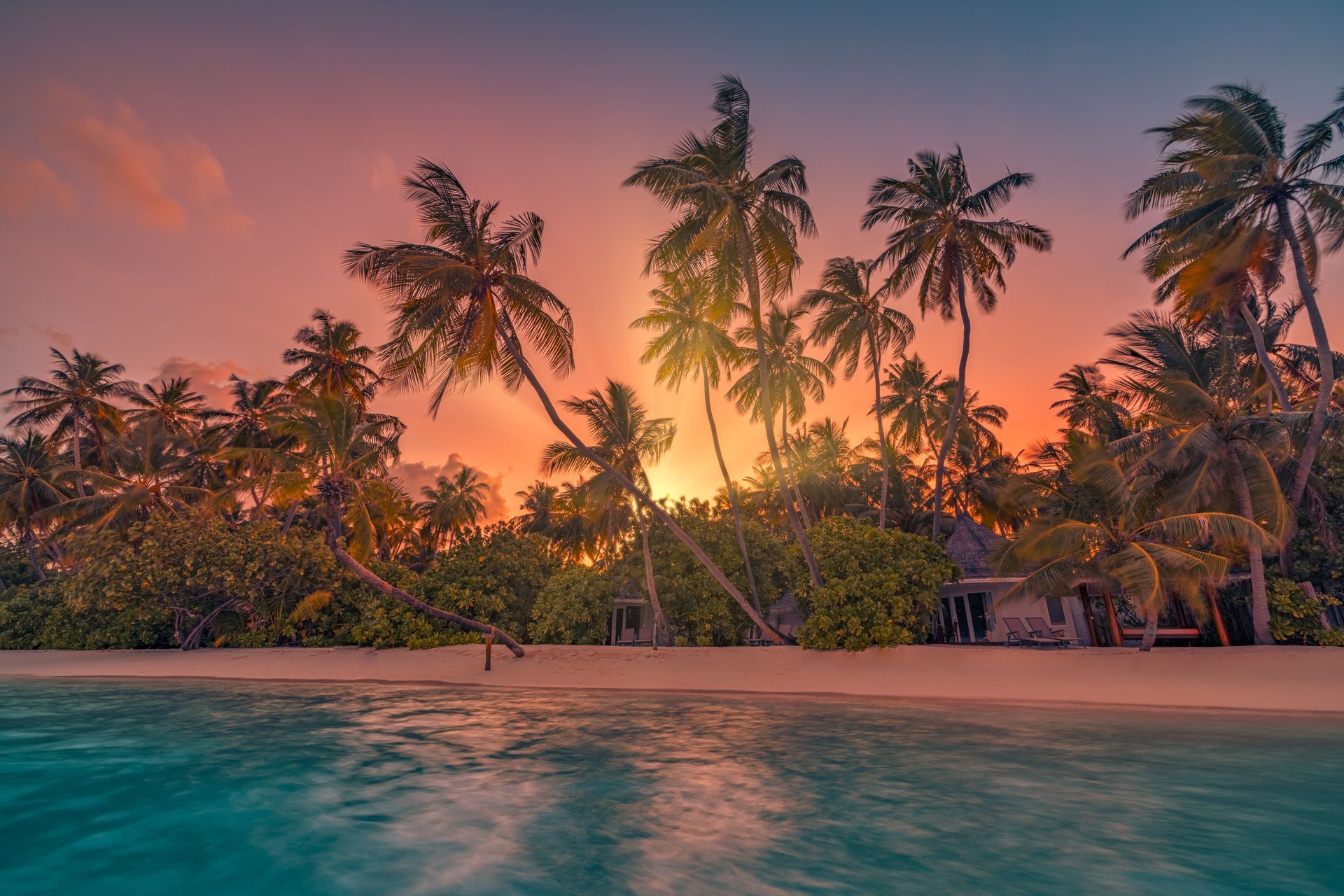A sunset over a tropical beach with palm trees and a swimming pool.