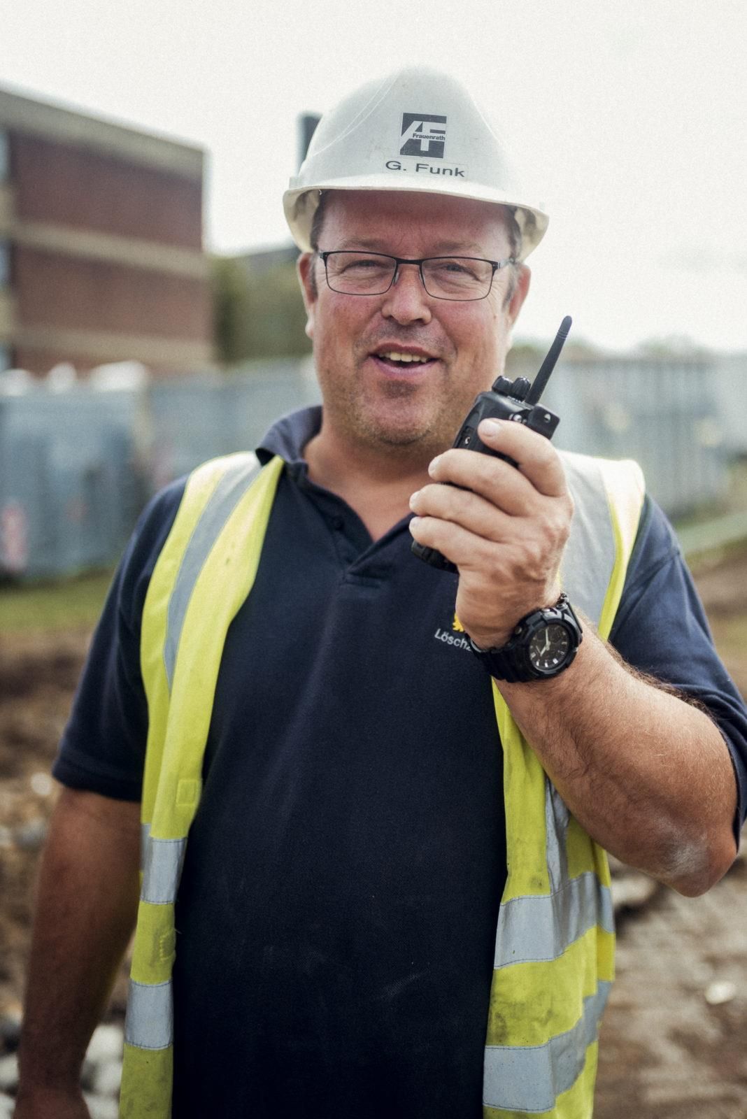 Ein Mann mit Schutzhelm und Sicherheitsweste hält ein Walkie-Talkie.