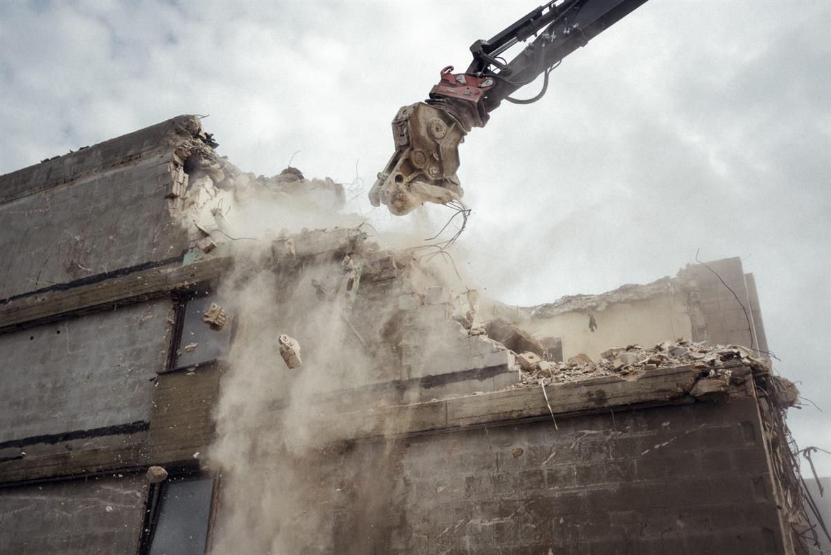 Ein Kran reißt ein Gebäude ab, wobei eine Menge Staub aufsteigt.