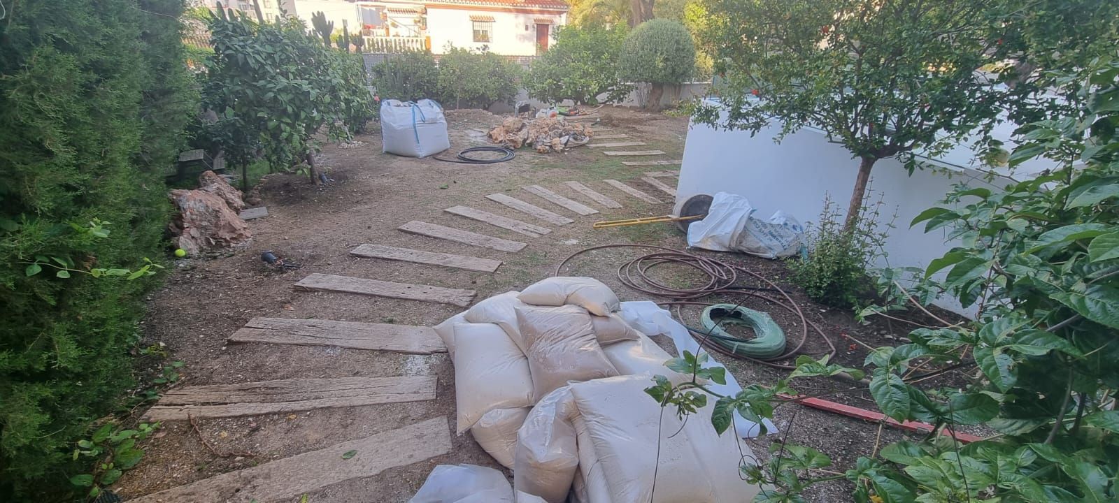 Un camino en un jardín con una pila de sacos de arena en el suelo.