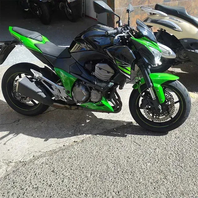 Una motocicleta verde y negra está estacionada al costado de la carretera.