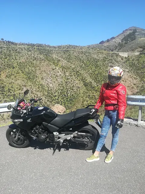 Una mujer con una chaqueta roja está parada junto a una motocicleta negra.
