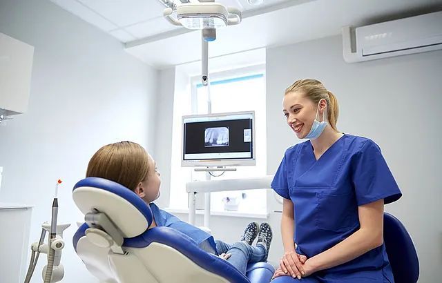 Una dentista está hablando con un paciente en una silla dental.