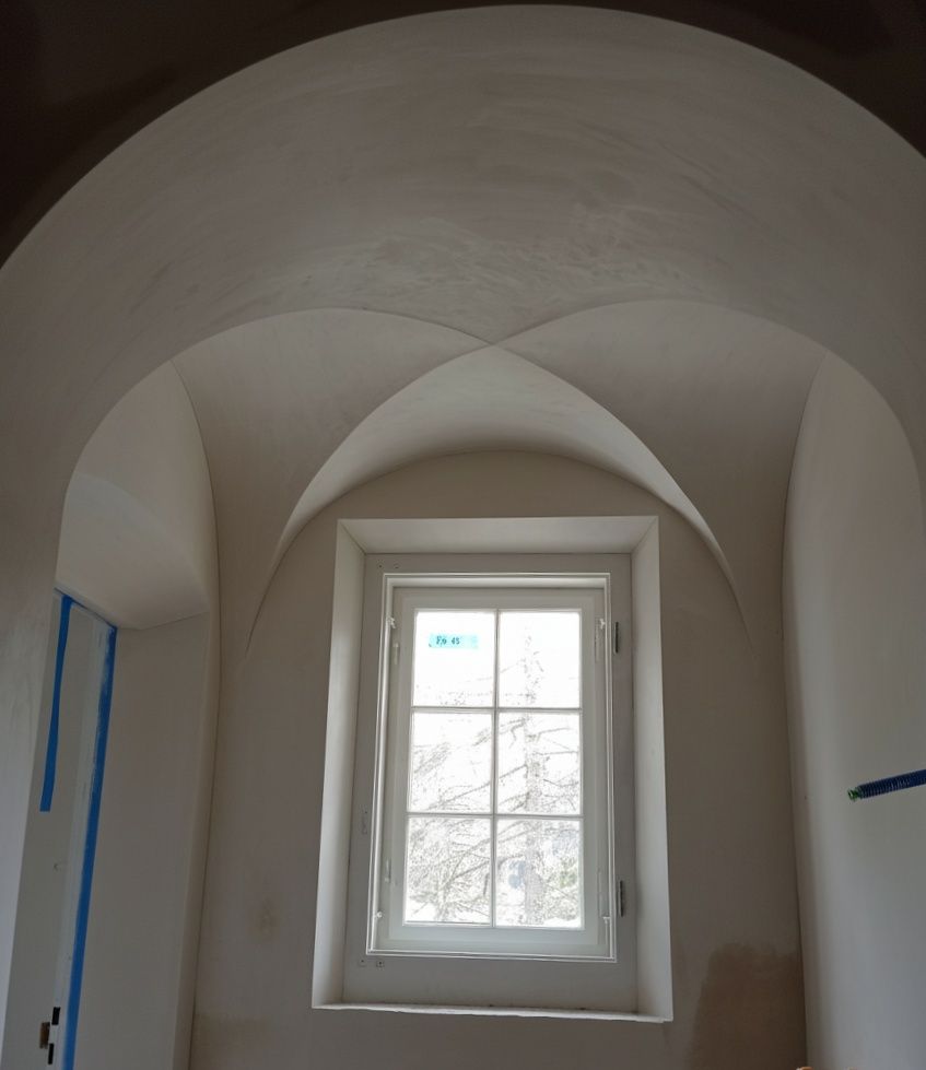 Innenansicht einer weissen Gewölbedecke über einem Fenster mit einfacher Sprossenscheibe, eingefasst in verputzte Wände.